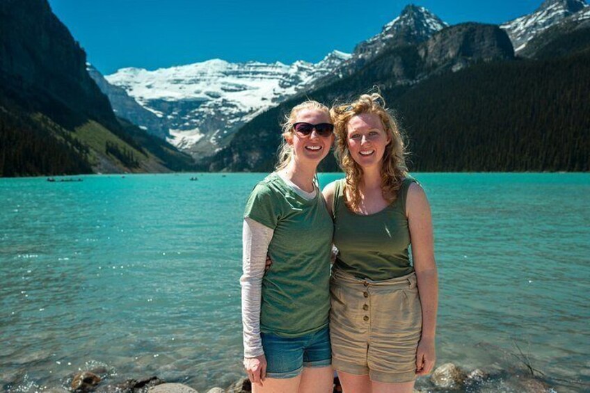 Two people standing by a turquoise lake with mountains in the background. 4