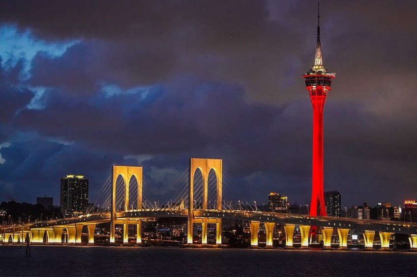 A bridge with two large arches and a tower with red lighting. 1