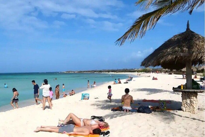 A beach with people sunbathing, a thatched umbrella, and a clear blue sky. 2
