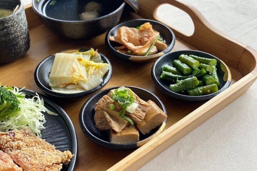 Una bandeja de madera con diferentes platos, incluyendo tofu, judías verdes y un trozo de pollo frito. 3