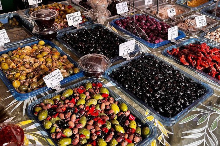 Une variété d’olives et de légumes marinés présentés dans des récipients transparents, chacun étant muni d’une étiquette indiquant le prix. 4