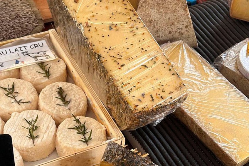 Un présentoir de fromages proposant différents types de fromages, notamment une grande meule et des meules plus petites, dont certaines sont décorées de brins de romarin. 2
