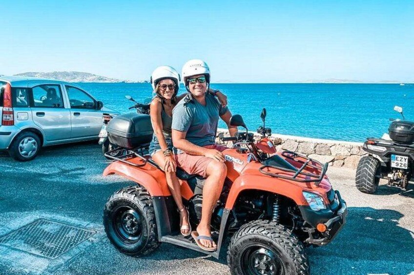 Een koppel op een oranje quadrijder aan zee, met een auto en nog een quadrijder op de achtergrond. 2