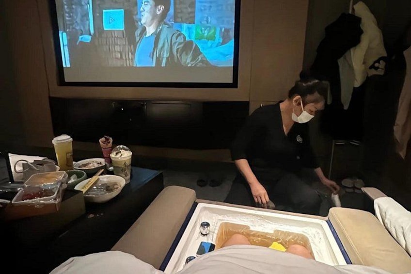 A person lying on a bed in a room with a television screen displaying a movie scene. 4