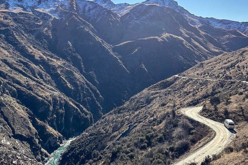 Una carretera sinuosa de montaña con un vehículo, terreno escarpado y un río. 5