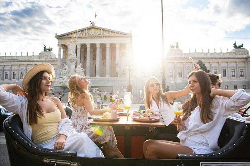A group of people sitting at a table with drinks and food, with a large building in the background. 3
