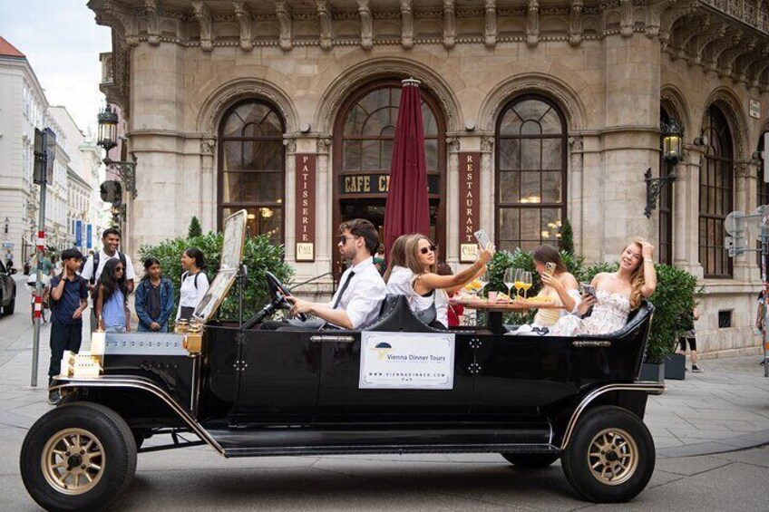 A vintage car with passengers taking photos in front of a cafe. 4