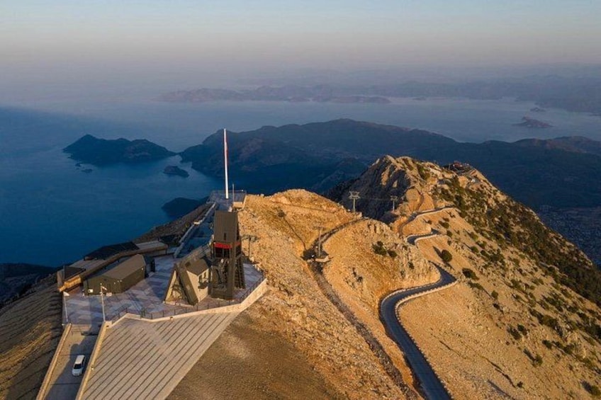 A mountainous landscape with a winding road, a tall structure, and a body of water in the distance. 5