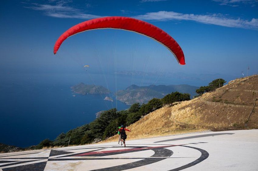 A person paragliding with a red canopy, a coastal landscape, and a clear sky. 2