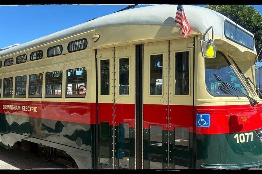 A vintage electric train with the number 1077, a wheelchair accessibility sign, and an American flag. 1