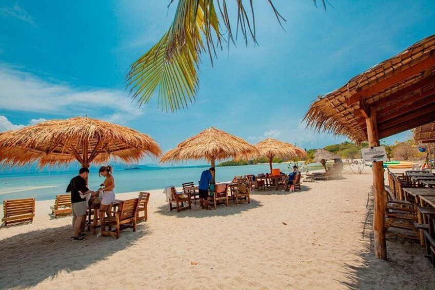 Ein Strand mit Reetsonnenstühlen, Holztischen und -stühlen. 3
