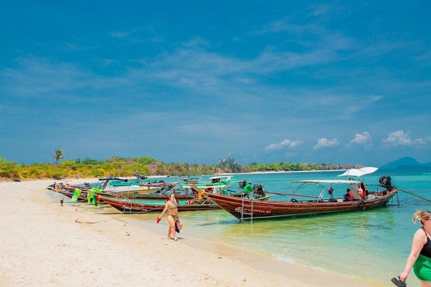 A beach with several boats docked, people walking, and a clear blue sky. 3