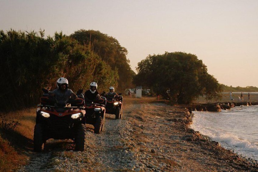 Three people riding ATVs on a gravel path by the water. 1