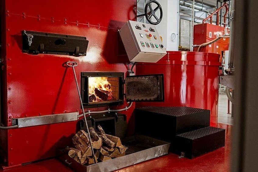Een rode industriële ketel met een bedieningspaneel, een vuurkamer en een stapelhout. 4