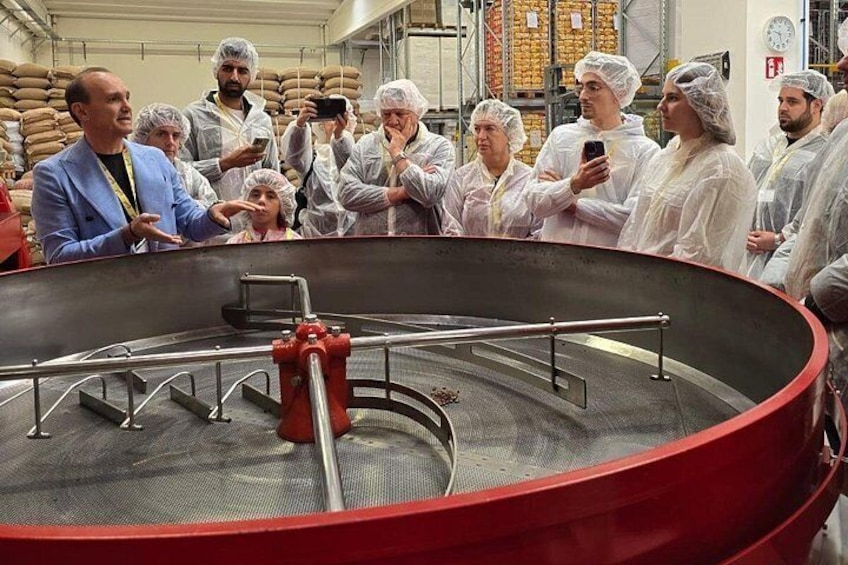 Een groep mensen in een grote industriële omgeving, die een ronde metalen constructie met een rode klep bekijken. 2