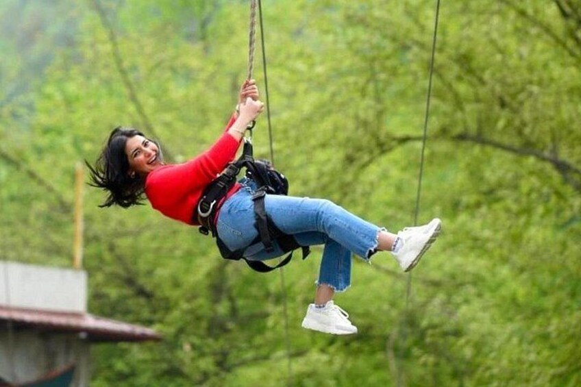En person åker på en zipline genom ett skogsområde. 4