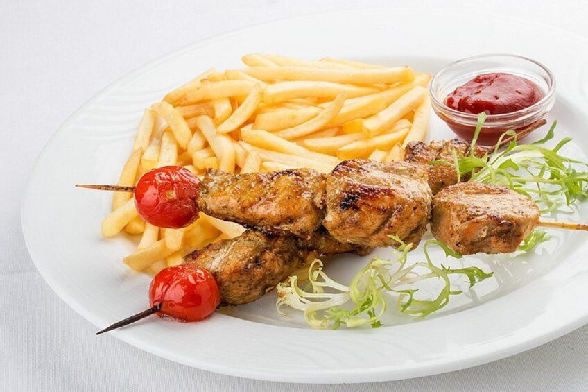 En tallrik med grillade köttspett, pommes frites, körsbärstomater och en liten skål med ketchup. 2