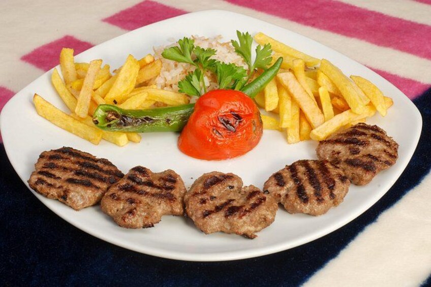 Une assiette contenant de la viande grillée, des frites, du riz, une tomate grillée et un poivron vert. 2
