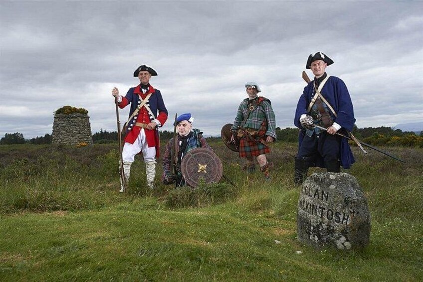 Reenactors in historical costumes, a stone monument, and a grassy field. 5