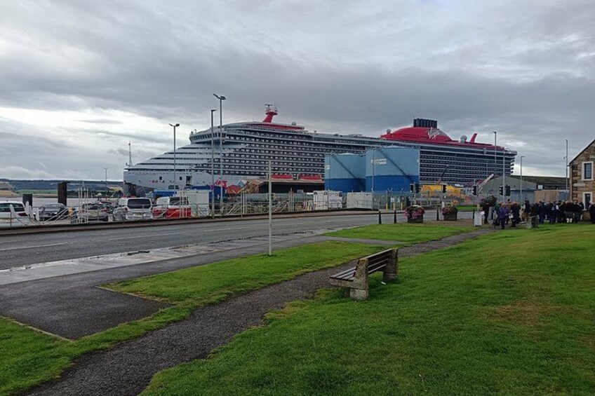 A cruise ship docked at a port with a grassy area and a bench in the foreground. 1