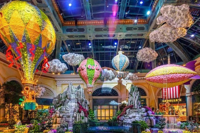 A large indoor atrium with a fountain, decorative hot air balloons, and hanging floral arrangements. 2