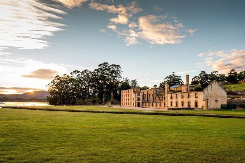 A historic building with a large lawn in front, a body of water in the background, and a sunset sky. 3