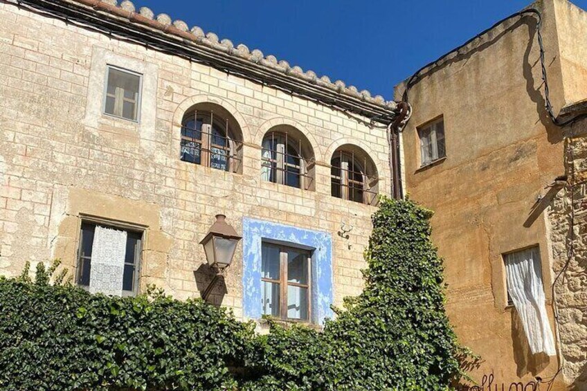 Un edificio histórico de piedra con ventanas de arco y una puerta azul, rodeado de vegetación. 5