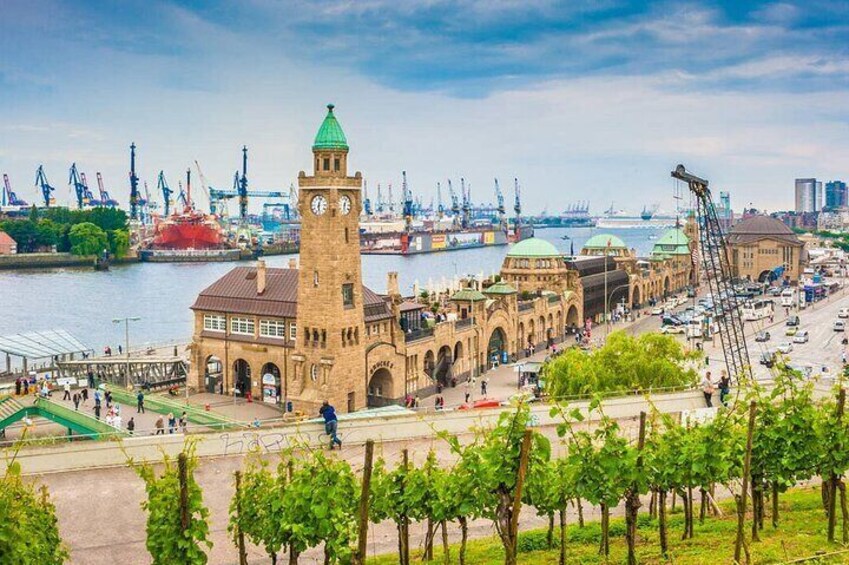 A historic building with a clock tower, a river, and industrial cranes in the background. 5