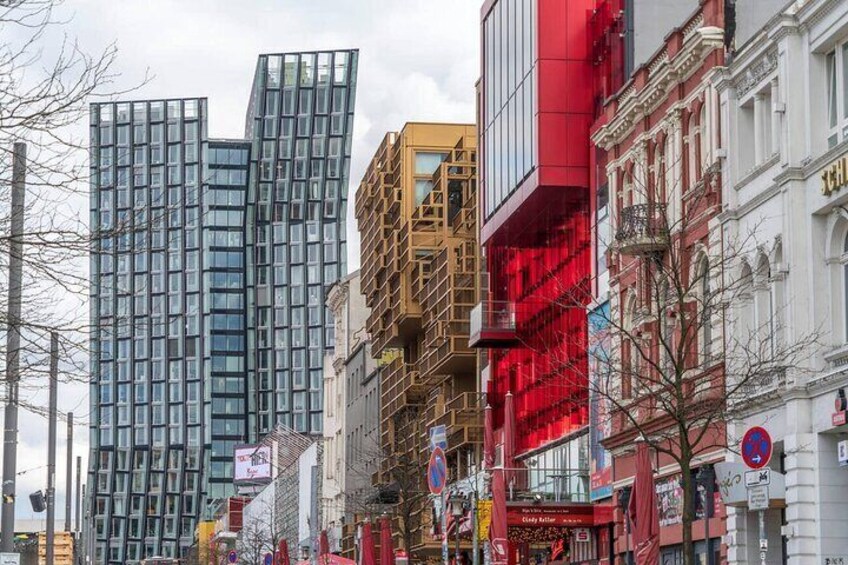 Une rue de la ville bordée de bâtiments modernes, dont un immeuble rouge avec des échafaudages et un grand bâtiment en verre. 1