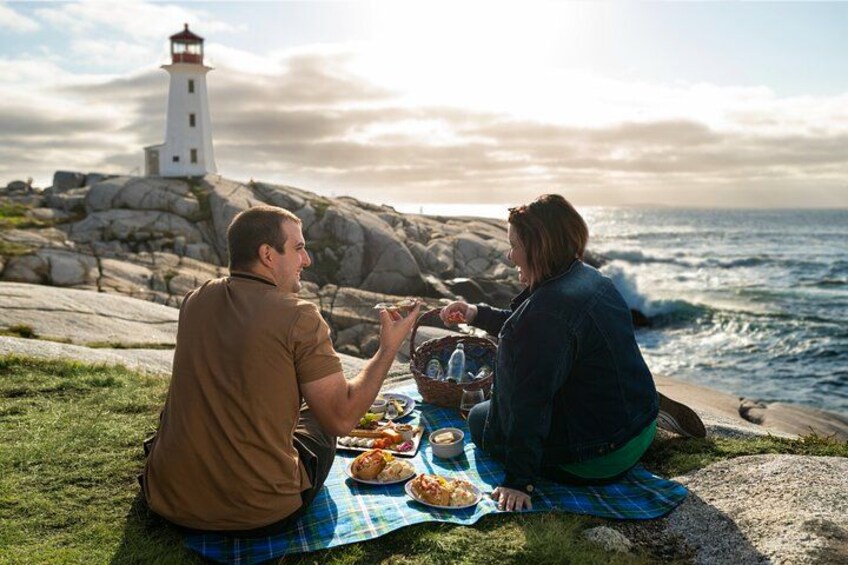 Two people sitting on a blanket by the ocean with a lighthouse in the background. 2