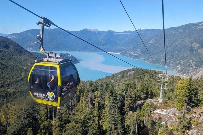 A cable car with 'SEA TO SKY' branding, a mountainous landscape, and a lake. 1