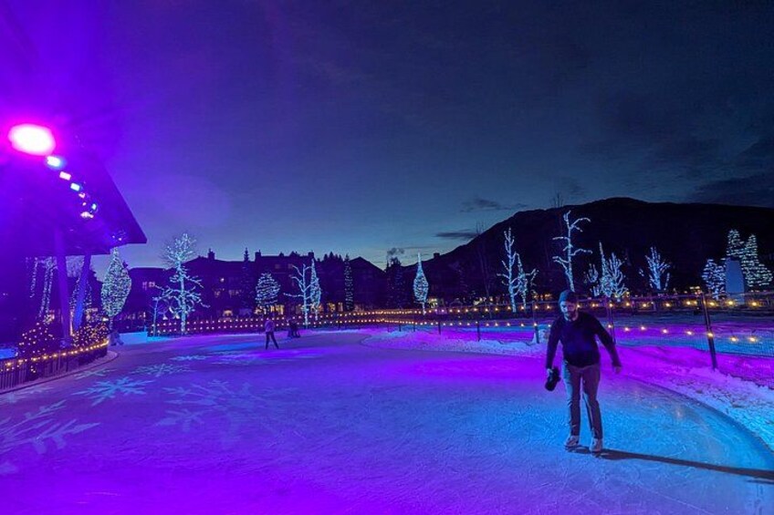 A person ice skating on a frozen surface with illuminated trees and buildings in the background. 4