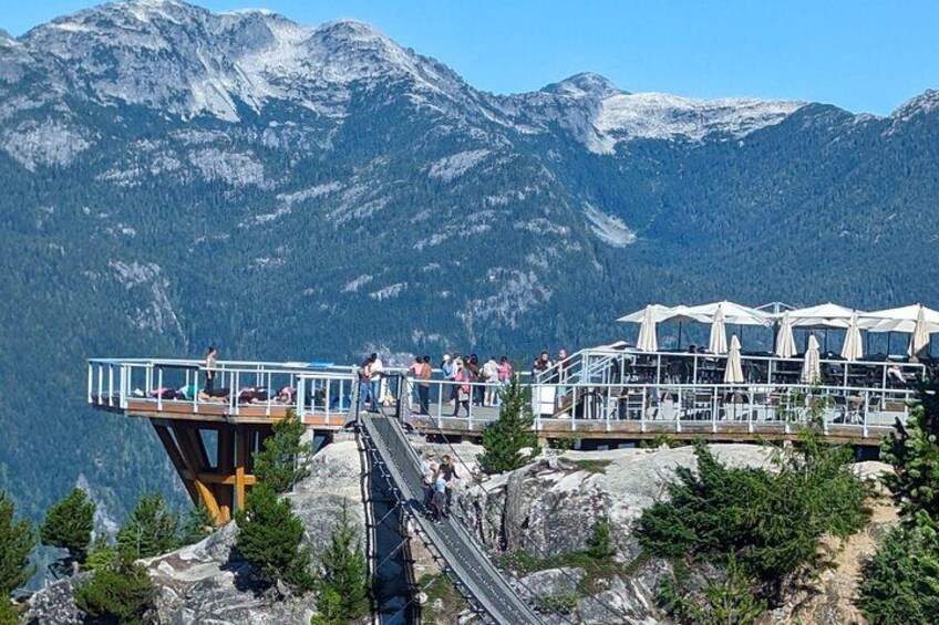 A wooden observation deck with a glass railing overlooking a mountainous landscape. 2