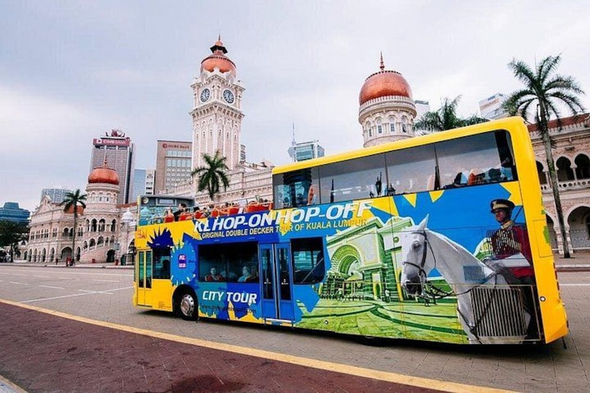 Un autobus à deux étages, orné d’une publicité colorée, est garé devant un bâtiment historique doté de coupoles. 1