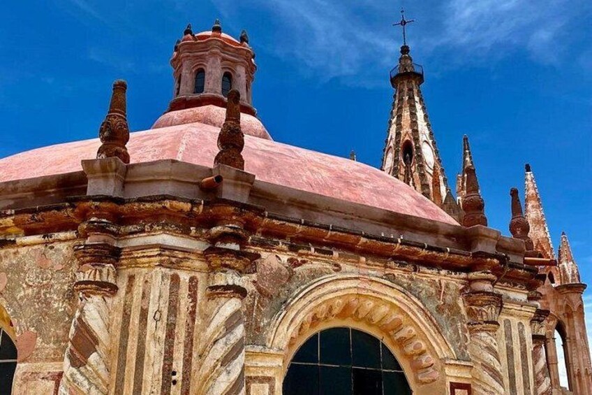 A historic building with a pink dome, intricate stone carvings, and a bell tower. 3