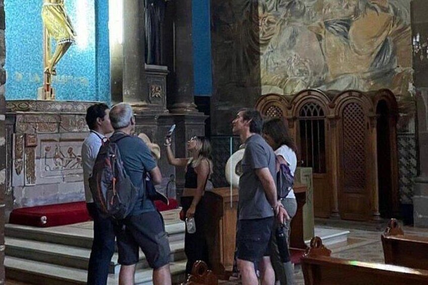 Een groep mensen in een kerk met een grote muurschildering en een gouden beeld. 5