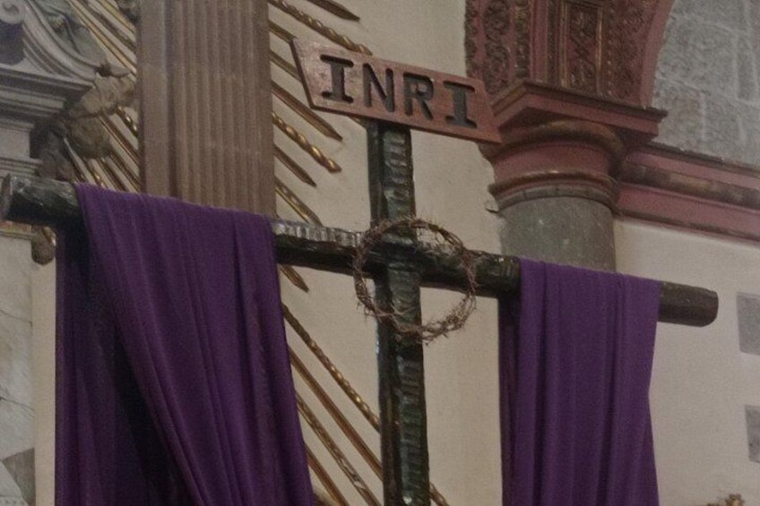 A cross with a sign reading 'INRI' and purple cloths draped over it. 5