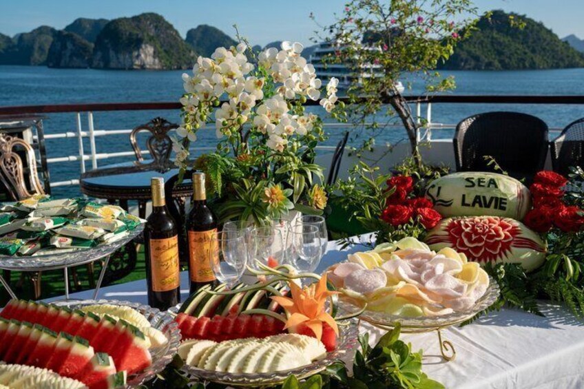 Een tafel met eten, bloemen en een bord waarop 'SEA LAVIE' staat, aan zee. 3