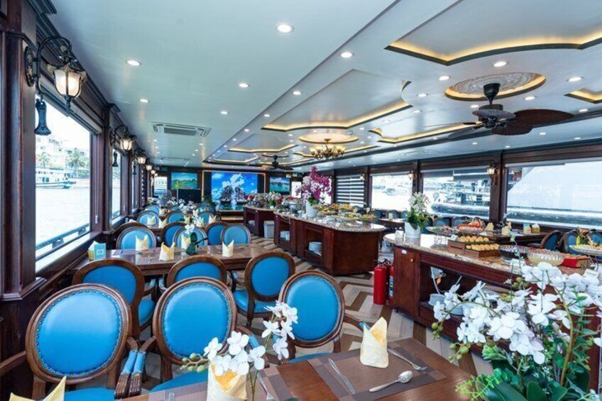 Een eetruimte op een schip met blauwe gestoffeerde stoelen, houten tafels en decoratieve bloemen. 5