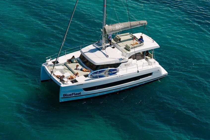 Een witte jacht genaamd 'BlueFleet' met 'BALI' op de zijkant, zeilt over turquoise water. 2