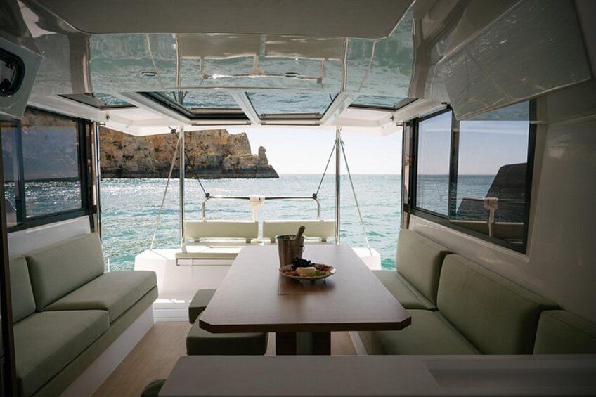 Bootinterieur met een tafel, kussens en uitzicht op zee en kliffen. 4