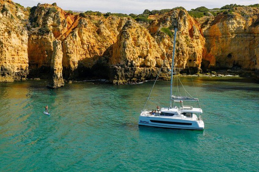 Een zeilboot op turquoise water, met rotsachtige kliffen op de achtergrond. 1
