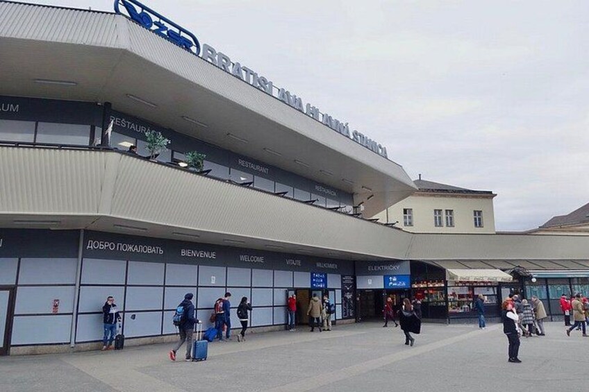 A modern building with a sign that reads 'BRATSMANN'. There are people walking and standing in front of the building, and a sign that says 'WELCOME'. 2