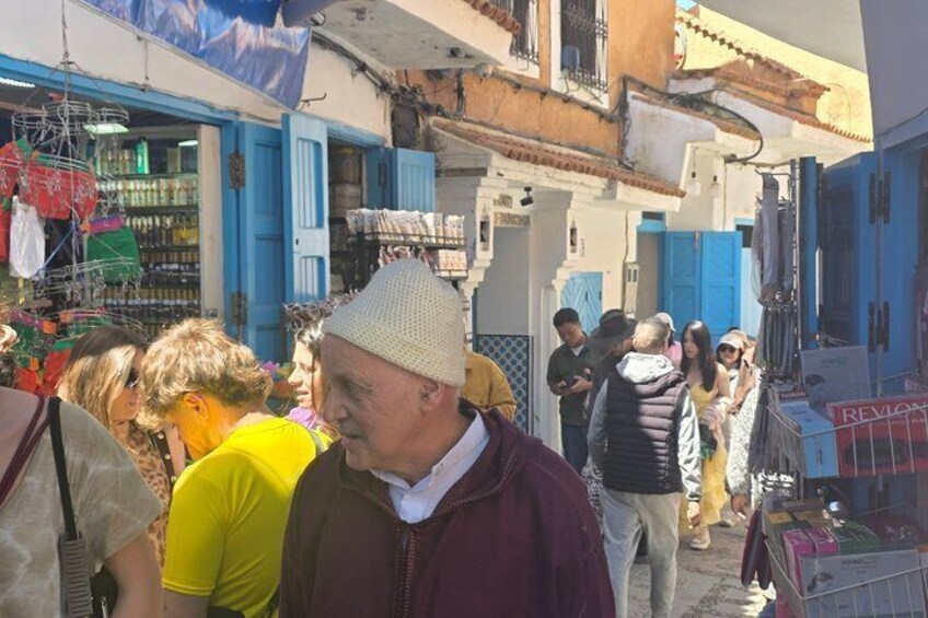 A crowded street with people, a man in a hat, and buildings with blue doors. 4