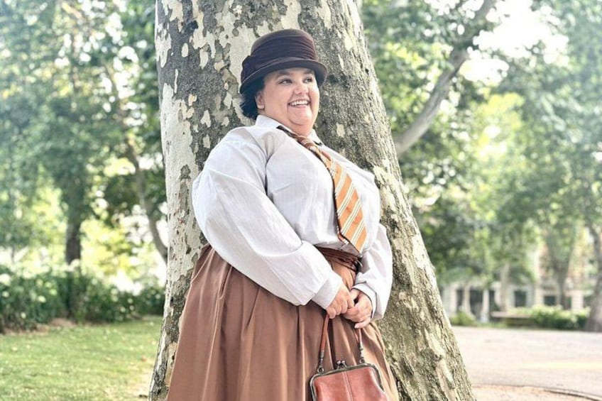 A person in traditional attire leaning against a tree in a park. 1