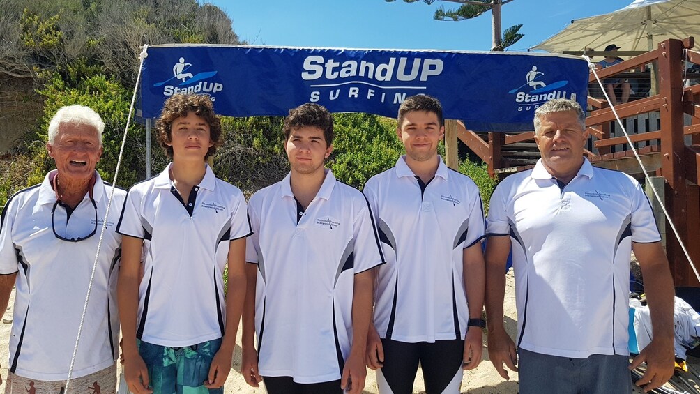 Five people in white shirts standing in front of a 'StandUP Surfing' banner. 5
