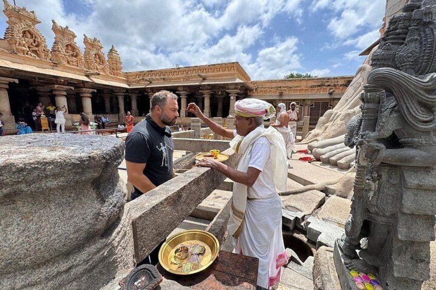 A man in traditional attire performing a ritual at a temple with intricate carvings and a large stone structure. 3