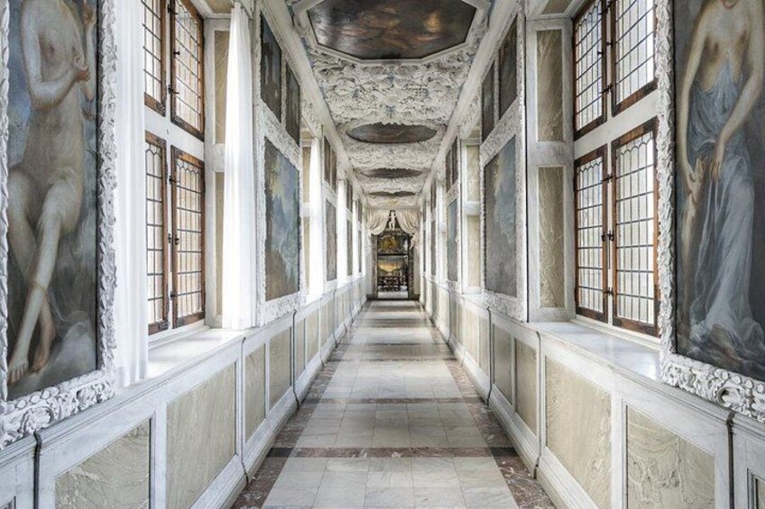 A long corridor with ornate columns, large windows, and detailed frescoes on the walls. 5