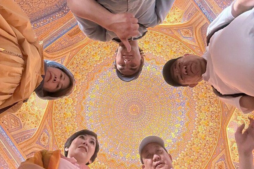Un gruppo di persone guarda verso un soffitto dettagliato e ricco di decorazioni, caratterizzato da un motivo geometrico. 5