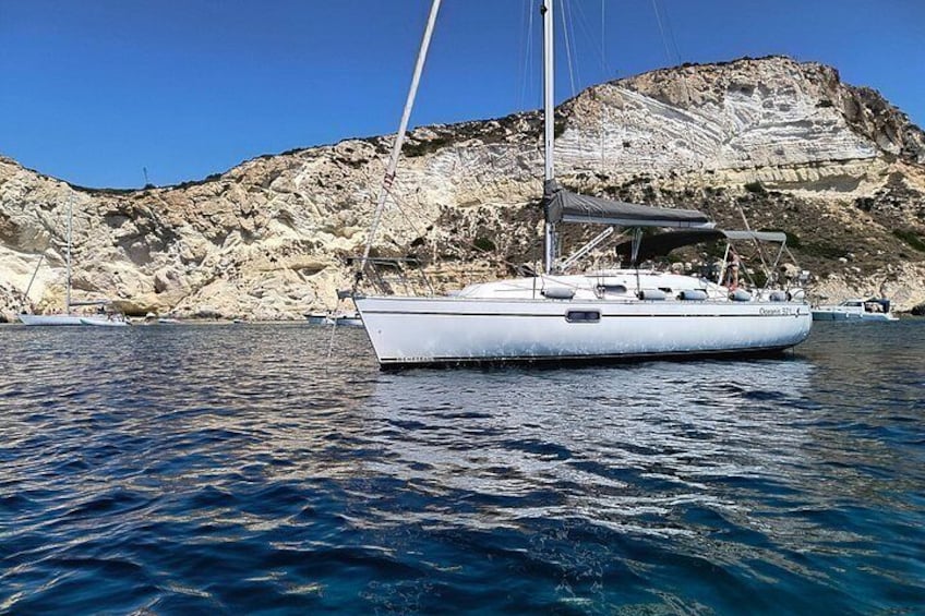 A white sailboat on calm water with a rocky coastline and cliffs in the background. 4